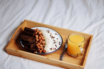 Delicious healthy Breakfast in the morning. Rye bread, banana, hazelnut, chocolate muesli, yogurt and fresh orange juice in a white bed, close up