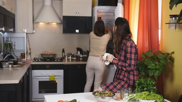 Two women drinking orange juice in the kitchen and feed each other fruits.