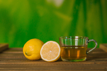 Glass Cup and lemons with tea on wooden table. Green background. Prevention of colds. Healthy diet.