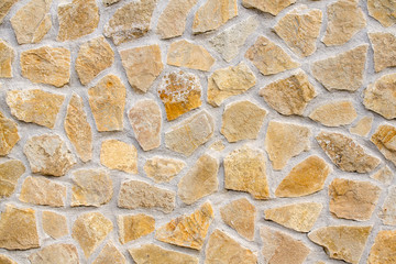 Pattern of decorative brown stone wall. Old castle wall background. Random size rock structure. Neatly stacked rough cut stone wall with concrete connection. Masonry wall of multicolored blocks.