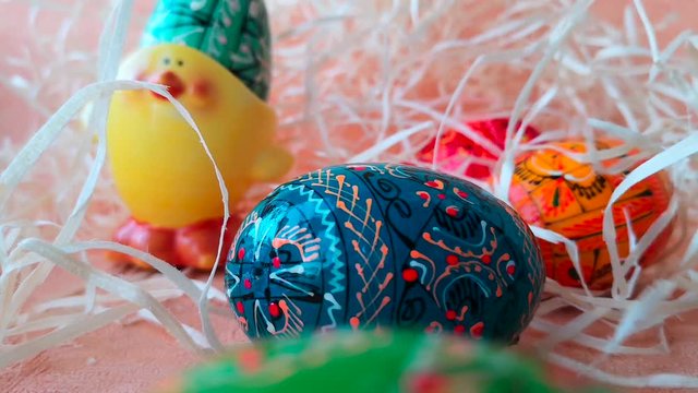 Happy Easter concept: multicolored painted Easter eggs and ceramic egg holder made in the shape of a chicken among decorative straw. The straw moves slightly in the wind.