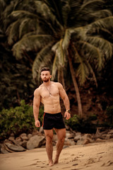 sexy handsome sportsman walking on the beach with palm trees in Thailand