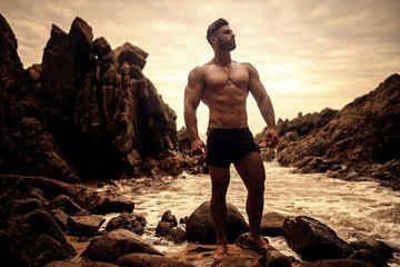 sexy handsome sportsman posing on the rocky beach in Thailand