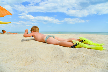 A cheerful and funny boy in flippers and a mask for scuba diving lies on the sand by the sea and...