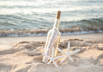 Fototapeta na wymiar pair of white starfish with happy birthday message in a bottle on beach sand