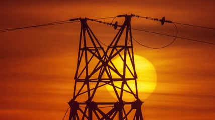 Sun setting behind power line pylon silhouette in dramatic red sunet sky background. Timelapse, 4K UHD.