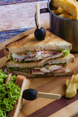 tasty chicken club sandwich with fries on wooden table