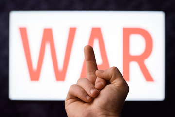 Young man not believing that third world war can start shows middle finger to a screen with inscription WAR