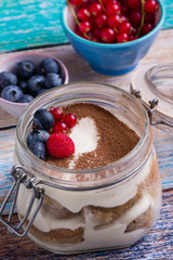 tasty tiramisu dessert in glass jar on color table