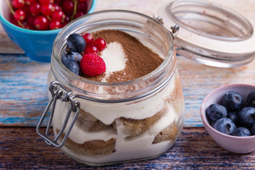 tasty tiramisu dessert in glass jar on color table