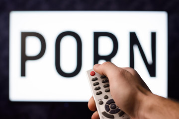 Young man having watched a ponography film pushes red power button on a remote controller of a TV...