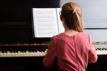 Little talented girl musician in a red dress playing the piano using folder with music sheet, performing beautiful classical music. Lifestyle concept. © Vitalii