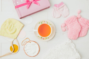 Using herbal breastfeeding tea to increase breast milk production for mothers concept. Different baby things with cup of tea on light white wooden board background, flat lay view studio composition