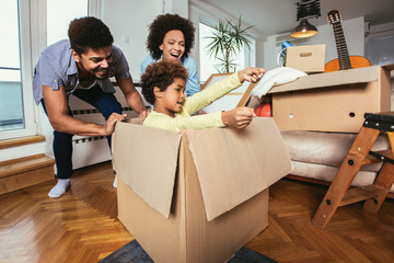 African American family, parents and daughter, unpacking boxes and moving into a new home, having...