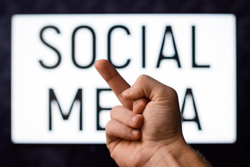 Man showing middle finger to a screen with inscription SOCIAL MEDIA. Symbol of disinformation of social medias