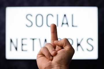 Man that doesn't use social networks shows middle finger to screen with inscription SOCIAL NETWORKS in order to show his attitude towards people who are depending on popular web sites and networks