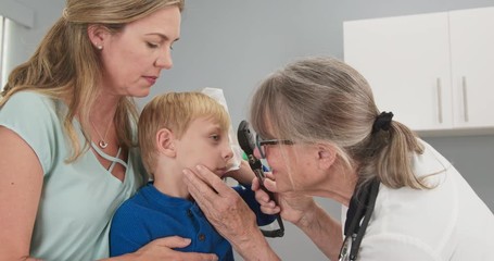 Child at pediatricians office holding ice pack on his head with mother and doctor checking concussion symptoms. Little boy using cold compress in medical exam room receiving first aid. Slow motion 4k