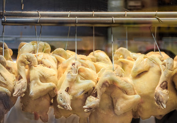 Whole poached chickens with heads hanging at a Hainanese Chicken Rice hawker stall in Singapore