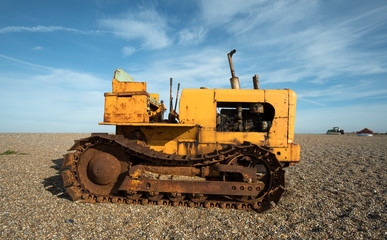 Old rusty yellow tractor unit on a pebble beach