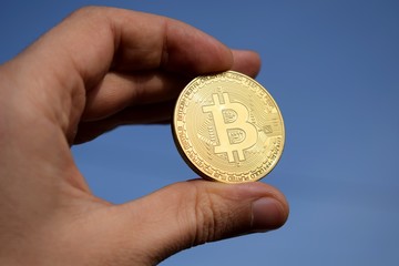 Hand holding golden bitcoin coin on blue sky background