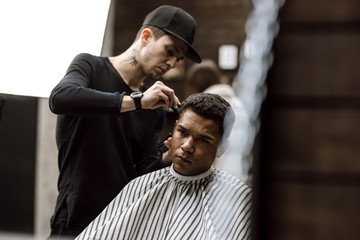 The barber dressed in black clothes  makes a razor cut hair back and sides for a stylish man...