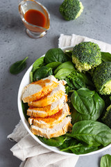 Chicken breast with spinach, broccoli and citrus dressing on a white plate. Grey concrete background. Copy space. Healthy diet lunch or dinner. Keto diet.