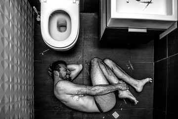Young man suffer by lying on floor in rest room. Drugs addiction. Hand ir wrapped with plait. Pills...