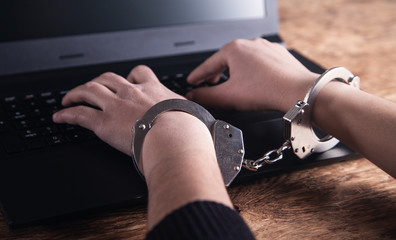 Hands in handcuffs typing on keyboard. Cyber Crime Concept