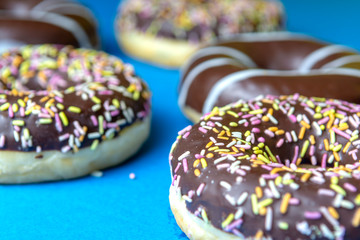 donuts covered with chocolate and sprinkled with decorative sprinkles on a blue background.