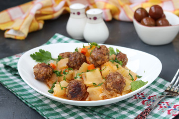 Stewed potatoes with meatballs on a white plate