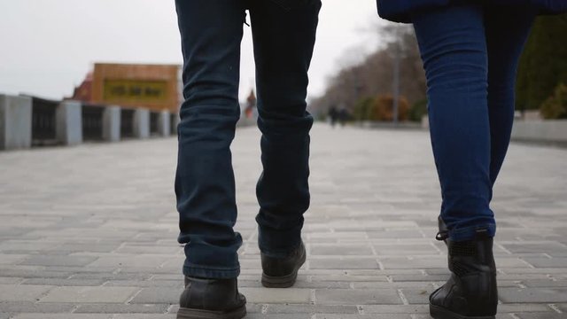 mother and baby legs in black boots walk down the sidewalk