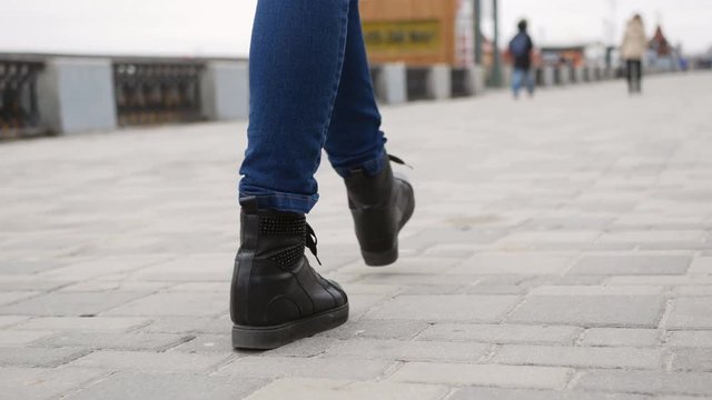 legs in black boots walk down the sidewalk