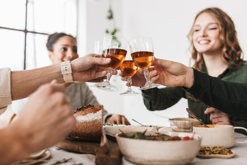 Close up group of international friends sitting at the table with glasses of wine in hands. Young colleagues joyfully celebrating together spending time on lunch in cozy cafe
