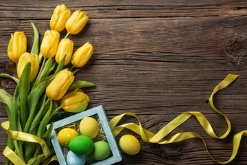 Yellow tulips in a paper bag, a nest with Easter eggs on a wooden background. Top view with copy space