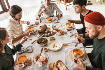 Top view of attractive international friends sitting at the table full of food eating together. Young colleagues having lunch dreamily spending time in cafe