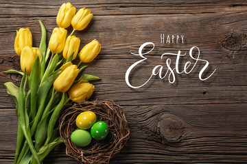 Yellow tulips in a paper bag, a nest with Easter eggs on a wooden background. Top view with copy space.