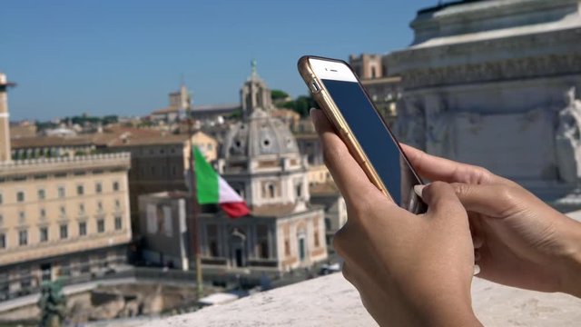 4K, Close up of a tourist asian woman holding and typing on mobile phone in famous landmark with Italian flag at Rome city. Girl check the smartphone and surfing in internet in Italy vacation. -Dan - Powered by Adobe