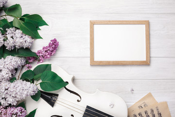 A bouquet of lilacs with violin, chalk board and music sheet on a white wooden table. Top wiev with space for your text