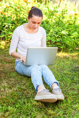 Freelance business concept. Young woman sitting on green grass lawn in city park working on laptop pc computer. Lifestyle authentic candid student girl studying outdoors. Mobile Office