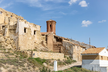 Fototapeta na wymiar old rustic houses and the Santa Cruz parish church in Plou town, province of Teruel, Aragon, Spain