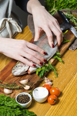 The chef stuffed raw trout with parsley and dill. Ingredients rosemary, lemon, tomatoes, garlic, salt, pepper. Black background, top view