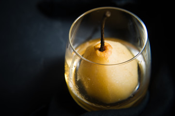 Pear poached in a glass, cooked on white wine. Black background, side view, space for text