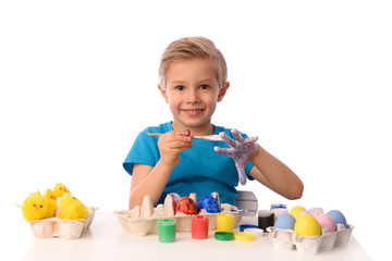 The child is painting Easter eggs. The boy is sitting at a table with colorful paints, his hands are dirty. She is happy, preparing for Easter. White isolated.