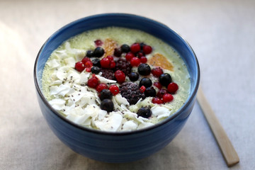 Fruit and vegetable smoothie (spinach, apple, banana, orange) with wild berries, chia seeds and coconut flake topping. Selective focus.