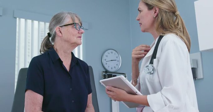 Senior patient talking with her reassuring doctor in exam room. Female primary care physician having conversation with older Caucasian woman during regular check up. Slow motion 4k
