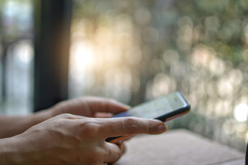 Close up people hands using smartphone in the cafe against blurred bokeh background. Selective focus with copy space.