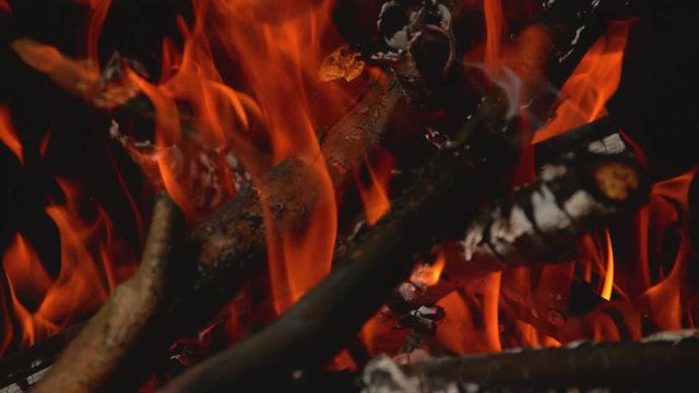 Time remap, macro, DOF cinematic shot of orange flames engulfing branches in a campfire