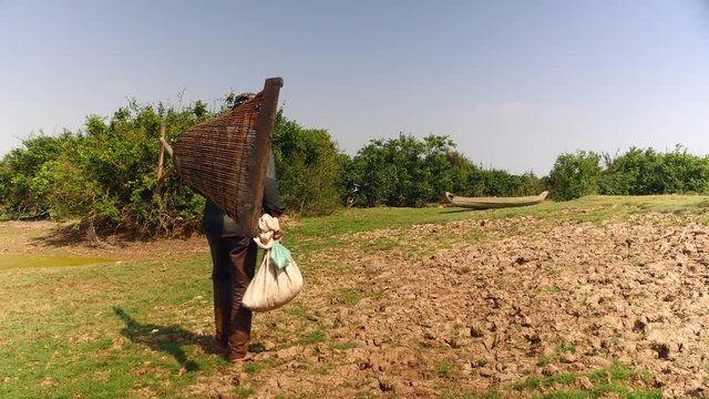 Fisher carrying his push basket and his plastic bag filled with clams through a field 