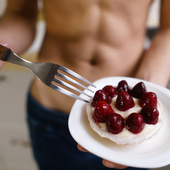balanced nutrition, diet, sugar free dessert, healthy food. young sporty man with muscle body eating tasty berry cake