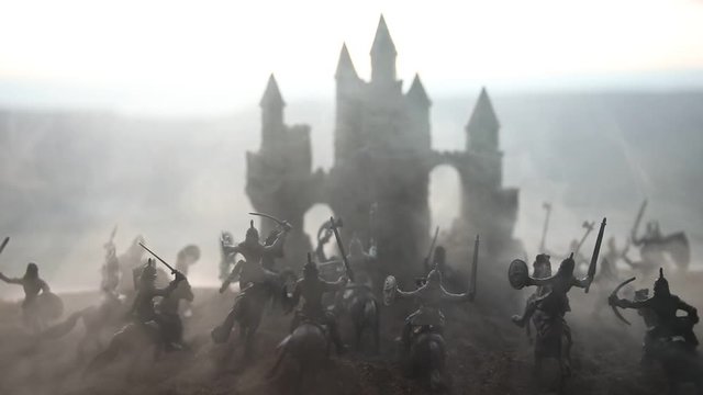 Medieval battle scene with cavalry and infantry. Silhouettes of figures as separate objects, fight between warriors on sunset foggy background. Selective focus